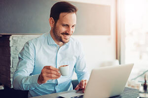 happy man sitting in front of a computer with a cup of espresso in hand