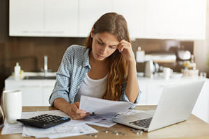 worried woman sitting over bills at table in front of computer