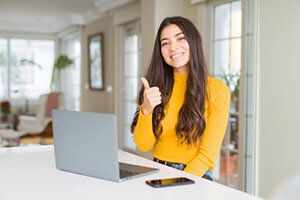 Satisfied woman with a raised thumb, sitting at the table on which there is a phone and a laptop